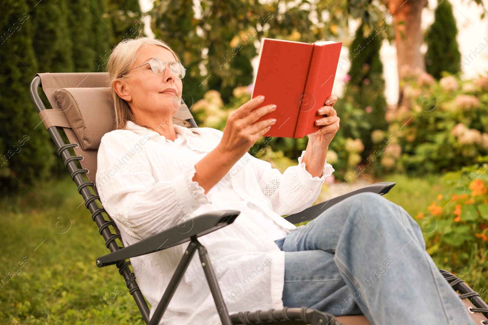 Photo of Senior woman reading book in armchair outdoors