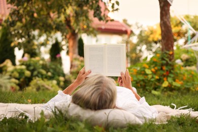 Photo of Senior woman reading book on blanket in garden