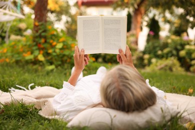 Photo of Senior woman reading book on blanket in garden