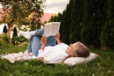 Photo of Senior woman reading book on blanket in garden