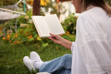Photo of Senior woman reading book on green grass in garden, closeup