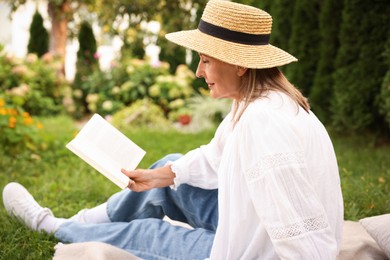 Photo of Senior woman reading book on blanket in garden