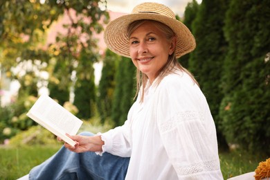 Photo of Senior woman reading book on green grass in garden