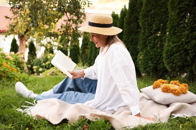 Photo of Senior woman reading book on blanket in garden