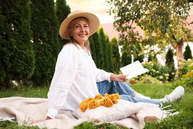 Photo of Senior woman reading book on blanket in garden