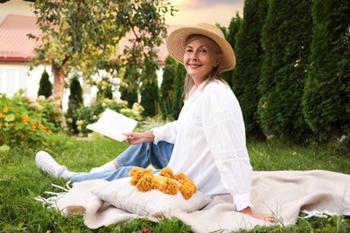 Photo of Senior woman reading book on blanket in garden