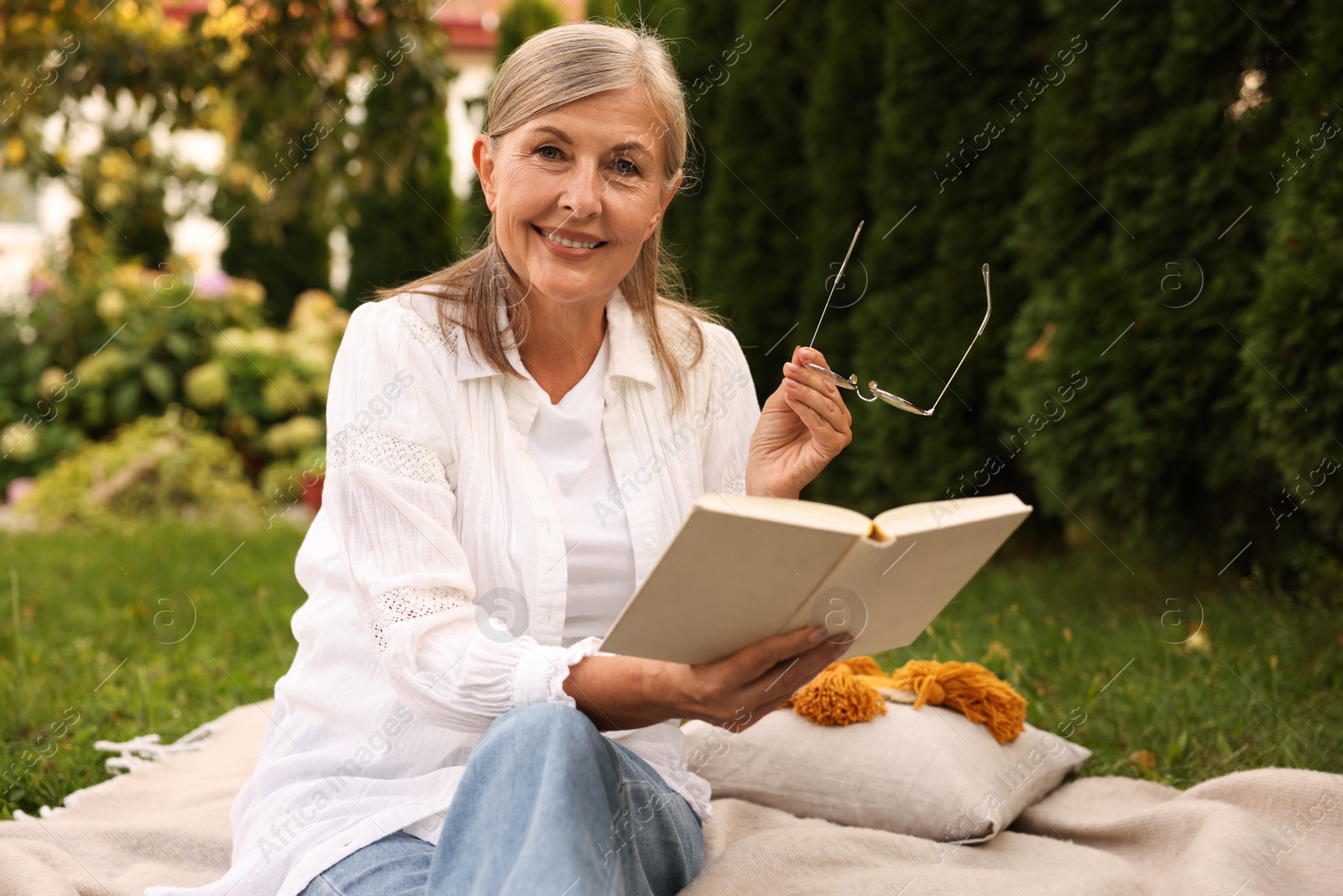 Photo of Senior woman reading book on blanket in garden