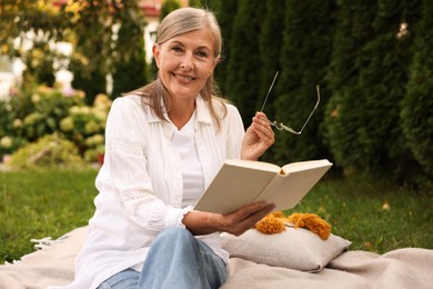 Photo of Senior woman reading book on blanket in garden