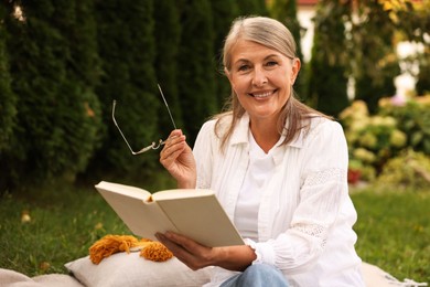Photo of Senior woman reading book on blanket in garden