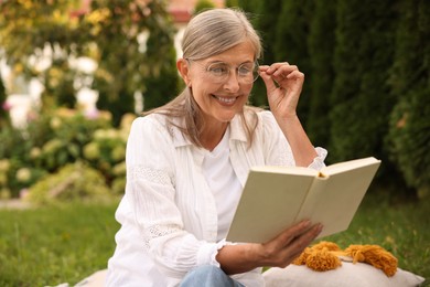 Photo of Senior woman reading book on green grass in garden