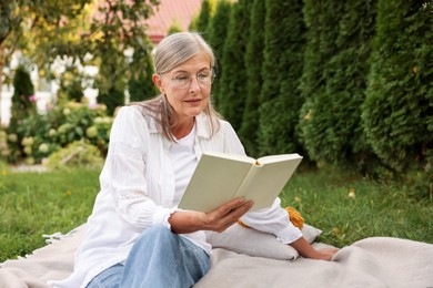 Photo of Senior woman reading book on blanket in garden