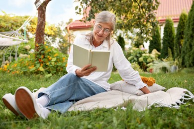 Photo of Senior woman reading book on blanket in garden