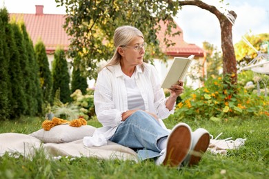 Photo of Senior woman reading book on blanket in garden