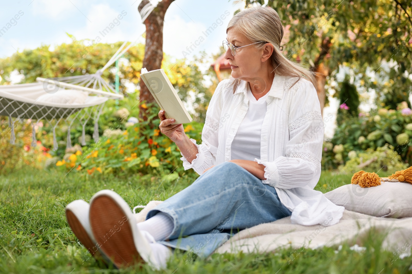 Photo of Senior woman reading book on blanket in garden