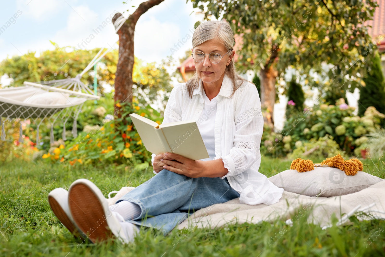 Photo of Senior woman reading book on blanket in garden