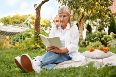 Photo of Senior woman reading book on blanket in garden