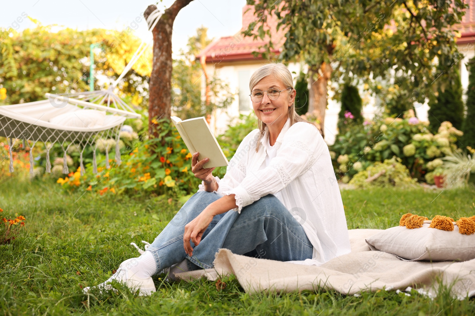 Photo of Senior woman reading book on blanket in garden