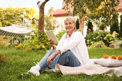 Photo of Senior woman reading book on blanket in garden