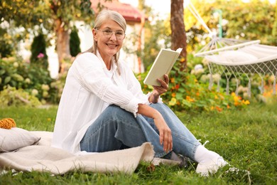 Photo of Senior woman reading book on blanket in garden
