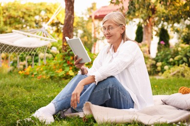 Photo of Senior woman reading book on blanket in garden