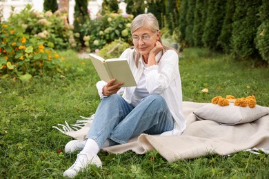 Photo of Senior woman reading book on blanket in garden