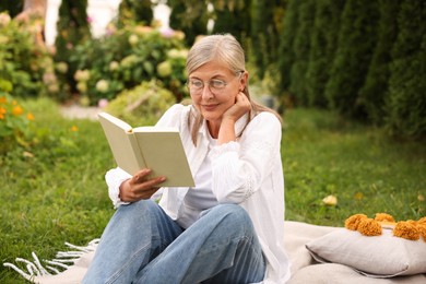 Photo of Senior woman reading book on blanket in garden