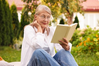 Photo of Senior woman reading book on green grass outdoors