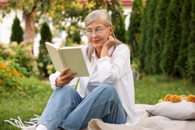 Photo of Senior woman reading book on blanket in garden