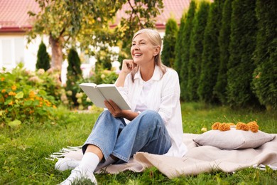 Photo of Senior woman reading book on blanket in garden