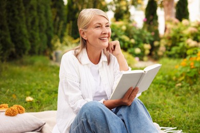 Photo of Senior woman reading book on blanket in garden