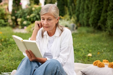Photo of Senior woman reading book on blanket in garden, space for text