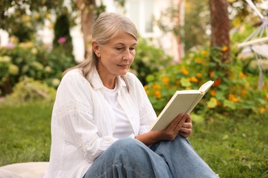 Photo of Senior woman reading book on green grass outdoors