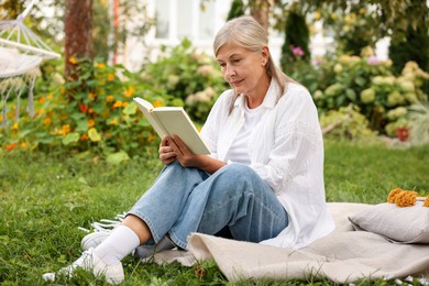 Photo of Senior woman reading book on blanket in garden