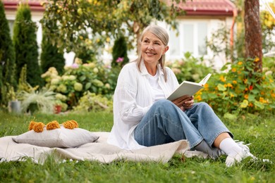 Photo of Senior woman reading book on blanket in garden, space for text