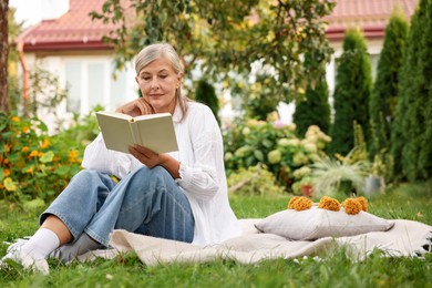 Photo of Senior woman reading book on blanket in garden, space for text