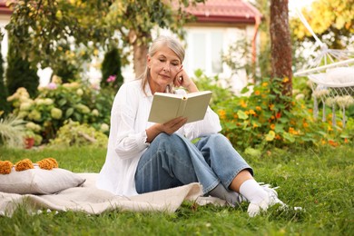 Photo of Senior woman reading book on blanket in garden