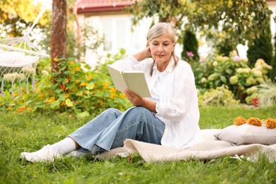 Photo of Senior woman reading book on blanket in garden
