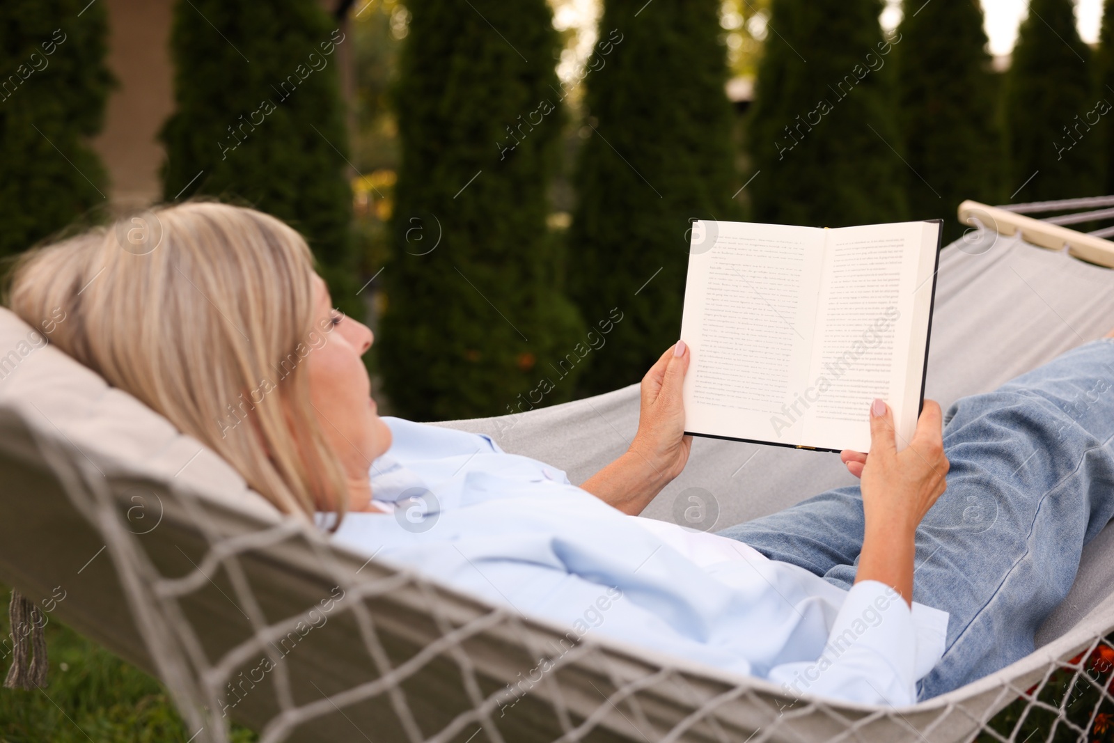 Photo of Senior woman reading book in hammock outdoors