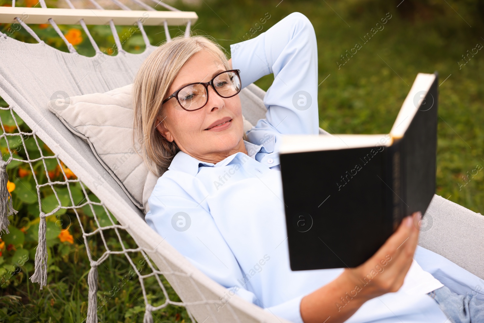 Photo of Senior woman reading book in hammock outdoors