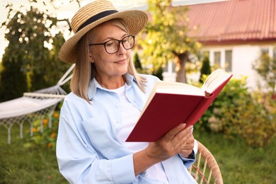 Photo of Senior woman reading book in wicker armchair outdoors