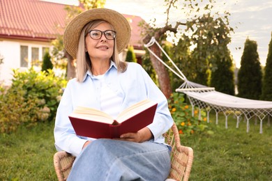 Photo of Senior woman reading book in wicker armchair outdoors