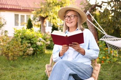 Photo of Senior woman reading book in wicker armchair outdoors, space for text