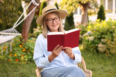 Photo of Senior woman reading book in wicker armchair outdoors