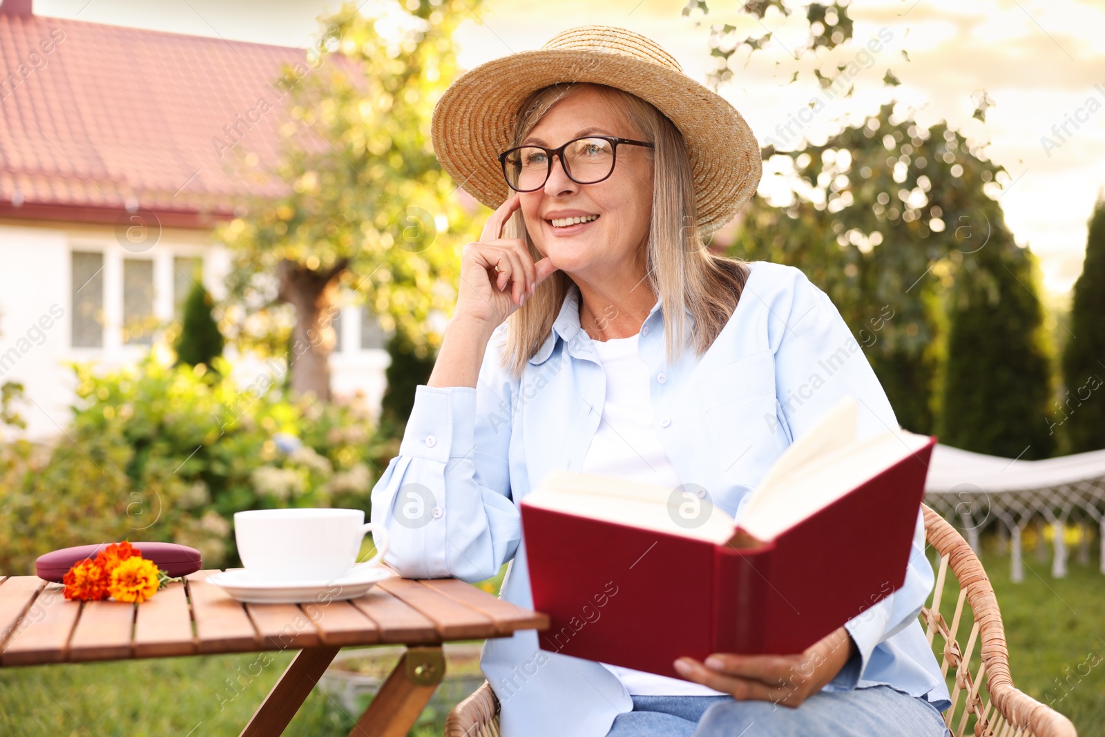 Photo of Senior woman reading book at wooden table in garden
