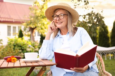 Photo of Senior woman reading book at wooden table in garden