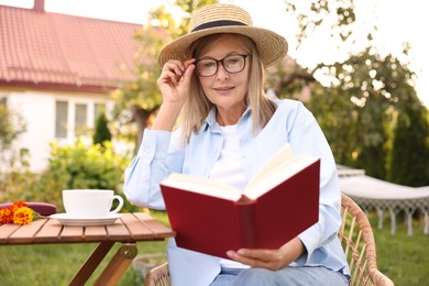 Photo of Senior woman reading book at wooden table in garden