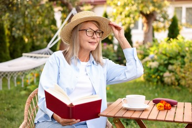 Photo of Senior woman reading book at wooden table in garden