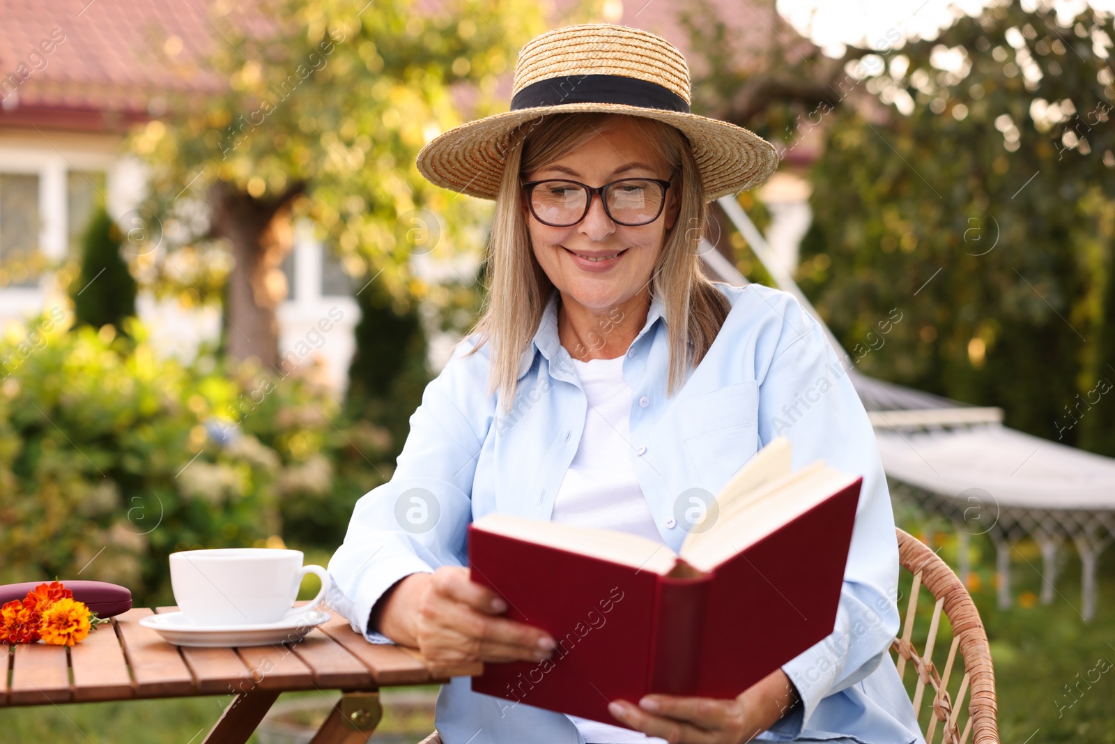 Photo of Senior woman reading book at wooden table in garden
