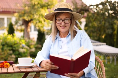 Photo of Senior woman reading book at wooden table in garden