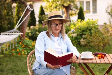 Photo of Senior woman reading book at wooden table in garden